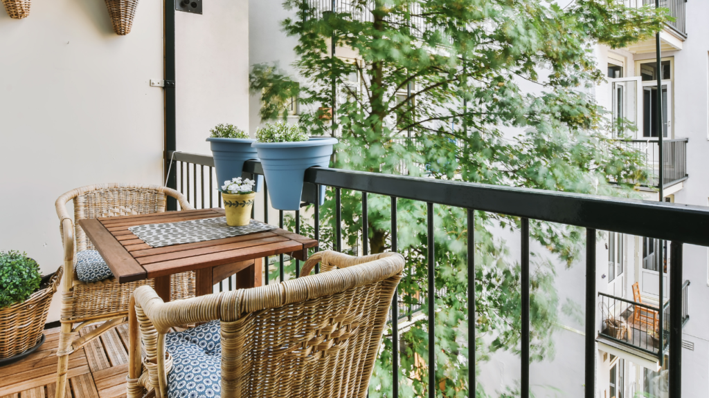 Gezellig balkon met houten tafel en rotan stoelen, versierd met planten in potten en uitzicht op een groene boom.