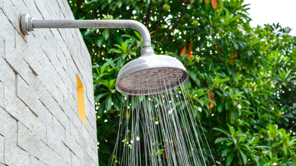 Boender Outdoor buitendouche met stromend water tegen een stenen muur en groene bomen op de achtergrond.