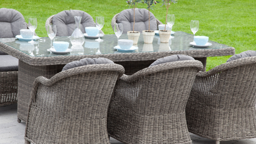 Boender Outdoor tuinset met gevlochten rotan stoelen en glazen tafel, gedekt met servies, op een terras met groene grasachtergrond