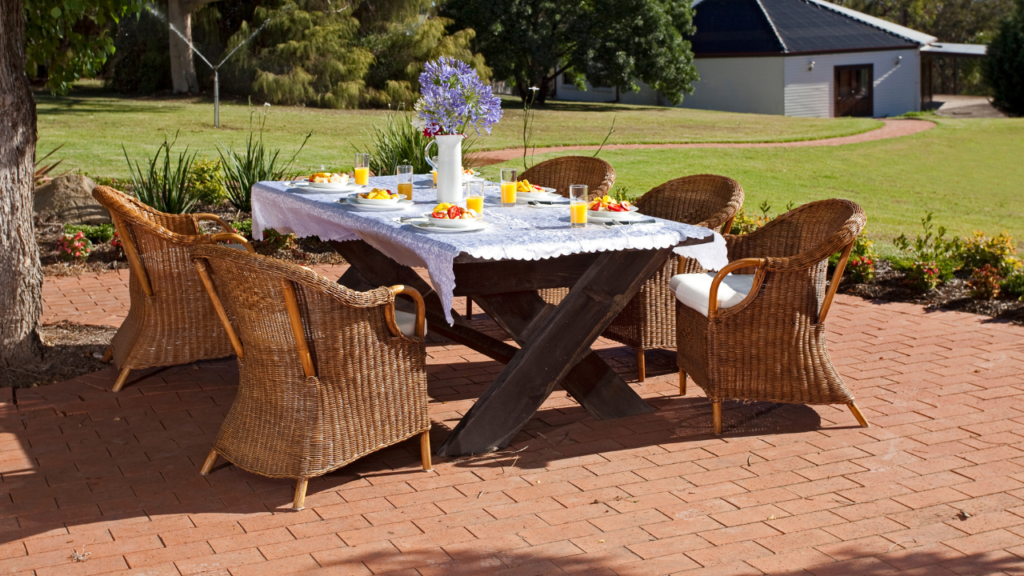 Boender Outdoor tuintafel met houten blad en gevlochten rotan stoelen, gedekt voor ontbijt in een zonnige tuin