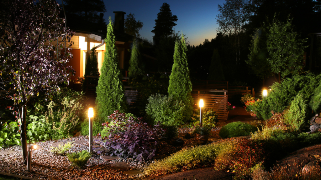 Verlichte tuin in de schemering met diverse planten en sierverlichting bij een huis, Boender Outdoor.