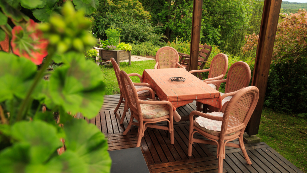 Houten tuinset met zes stoelen en een tafel op een terras, omringd door groene tuinplanten en bomen