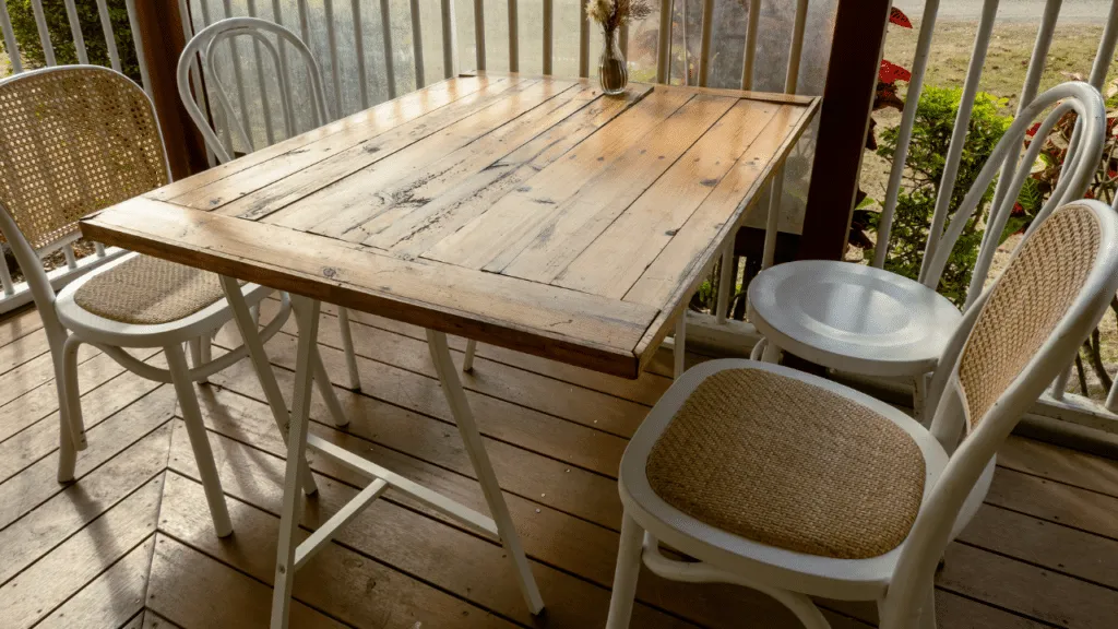 Rustieke houten tuintafel met vier witte stoelen op een veranda, ideaal voor een gezellige tuinsetting