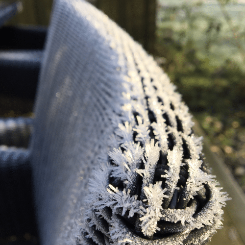 Close-up van een wicker tuinstoel bedekt met een laagje rijp in een koude winterse ochtend.