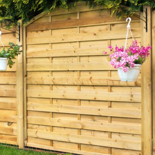 Houten tuinschutting met bloeiende roze bloemen in een witte hangpot tegen een groene achtergrond