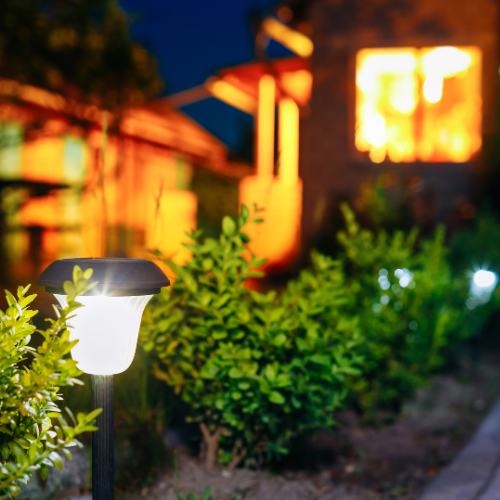 Tuinpad met LED-solarlamp en groene struiken bij een sfeervol verlichte woning in de avond