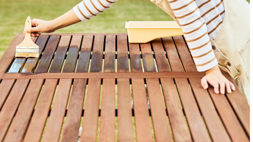 Houten tuintafel wordt geolied met een brede kwast voor onderhoud