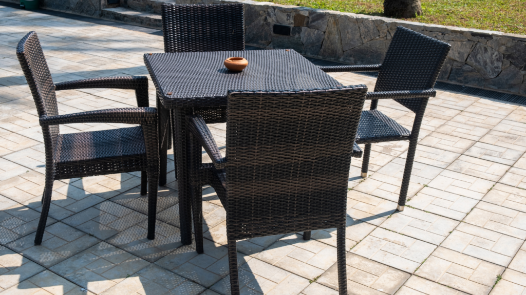 Wicker tuinset met zwarte tafel en stoelen op een betegeld terras, ideaal voor buitengebruik in alle seizoenen