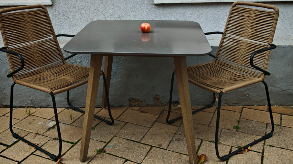 Minimalistische tuintafel met houten poten en twee gevlochten stoelen met appel als detail