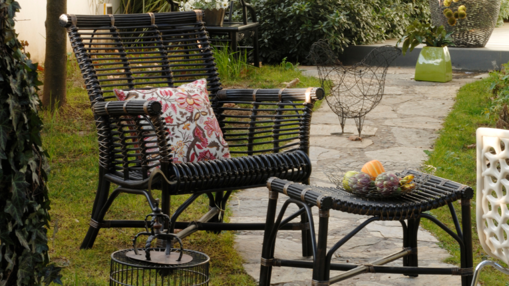 Zwarte rotan tuinstoel met kleurrijk kussen naast lage tafel met fruitmand in tuinpad setting