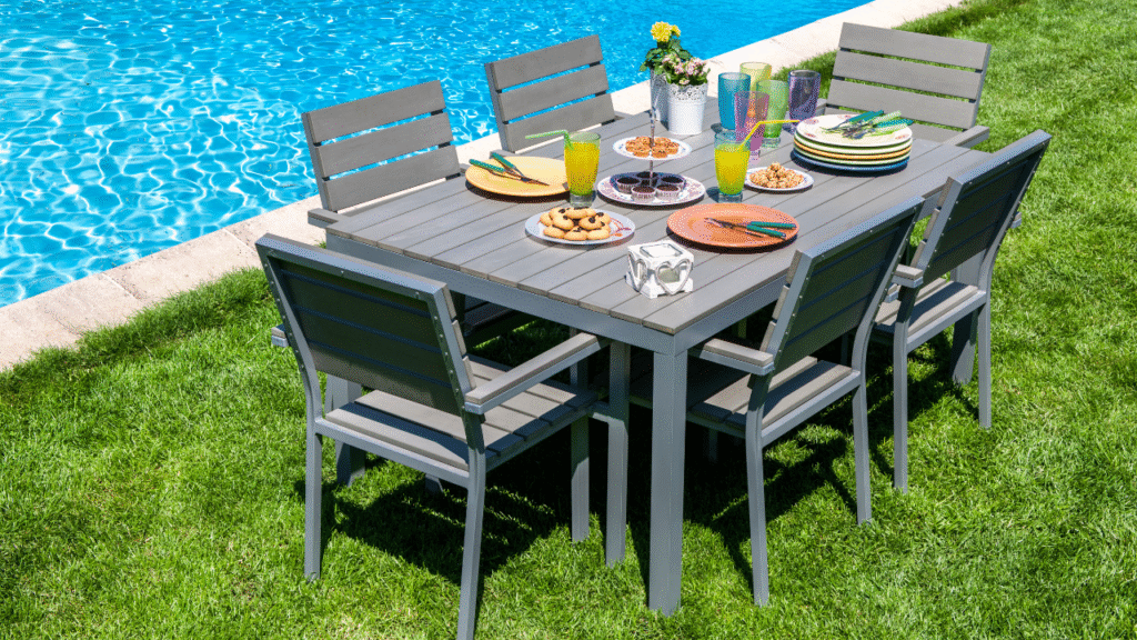 Grijze tuinset met zes stoelen en een gedekte tafel met drankjes en snacks naast een zwembad