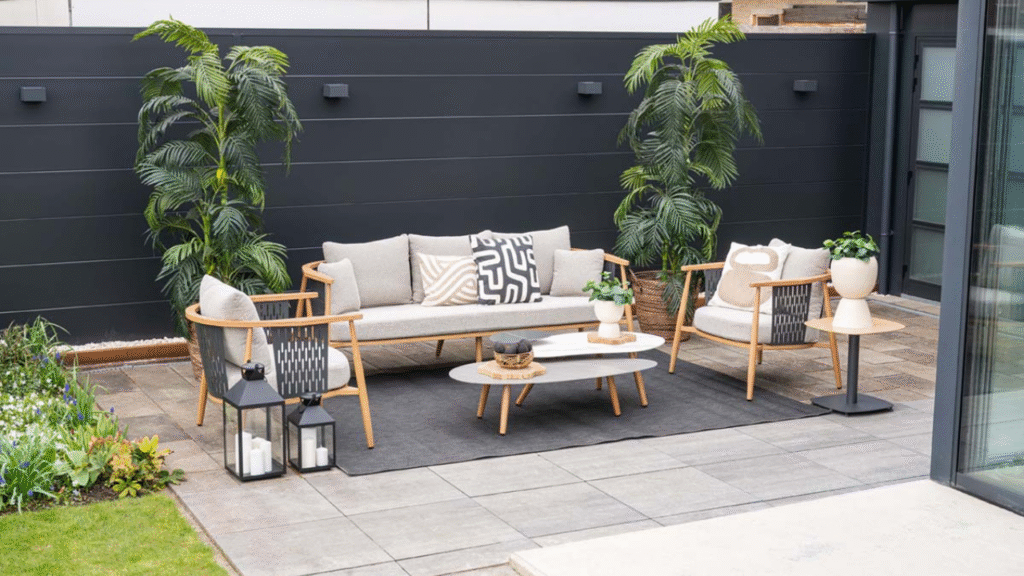 Moderne loungeset met houten frame en lichte kussens op strak terras met zwarte schutting